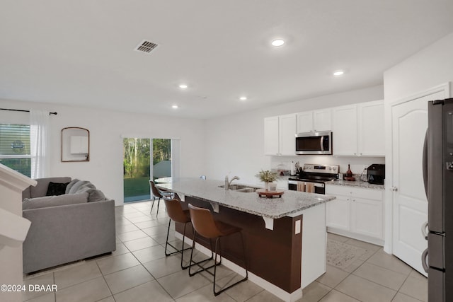 kitchen with light stone counters, stainless steel appliances, white cabinetry, a breakfast bar, and a kitchen island with sink