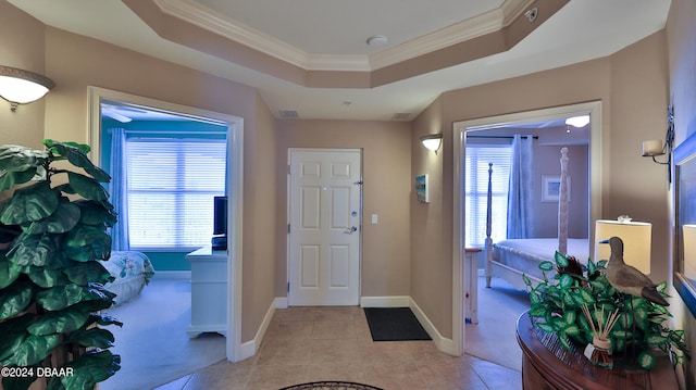 entryway with ornamental molding, light tile patterned flooring, and a tray ceiling