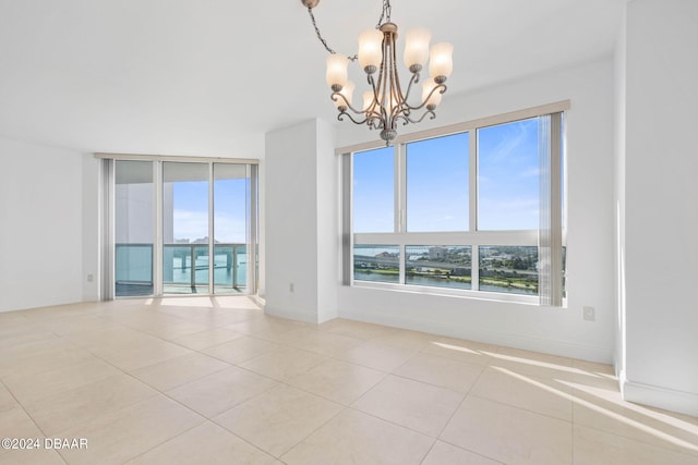 empty room featuring a water view, a healthy amount of sunlight, a chandelier, and light tile patterned floors