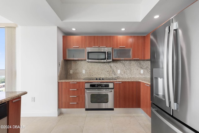 kitchen with decorative backsplash, appliances with stainless steel finishes, light tile patterned flooring, and light stone countertops