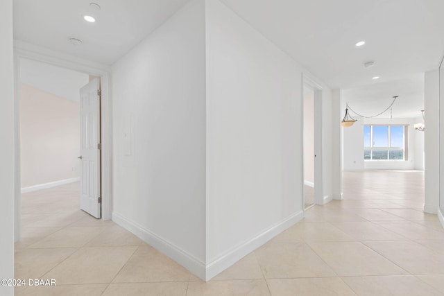 corridor with light tile patterned floors and a notable chandelier