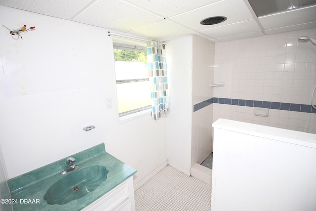 bathroom with a drop ceiling, tile patterned flooring, vanity, and a tile shower