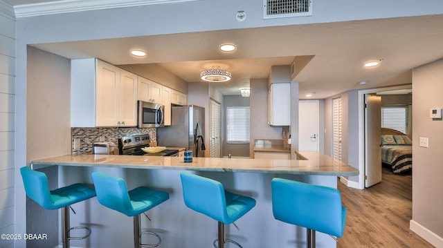 4601 S Atlantic Ave Unit 702, Ponce Inlet, FL 32127 - kitchen with visible vents, appliances with stainless steel finishes, light wood-type flooring, white cabinets, and a peninsula