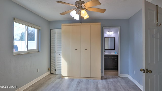 unfurnished bedroom with two closets, ensuite bath, ceiling fan, and light hardwood / wood-style flooring