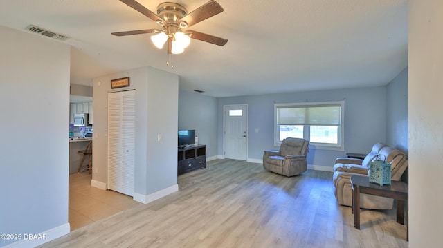 living area with a ceiling fan, visible vents, baseboards, and wood finished floors