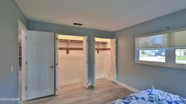 bedroom featuring baseboards, visible vents, two closets, and wood finished floors