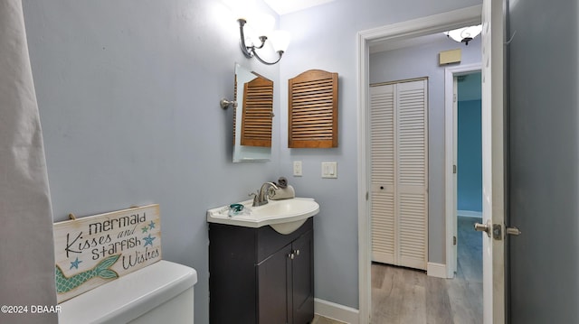 bathroom featuring baseboards, toilet, wood finished floors, vanity, and a closet