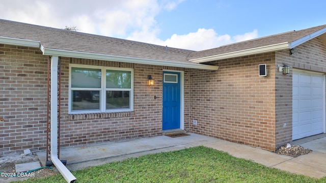 property entrance featuring a garage, brick siding, and a shingled roof