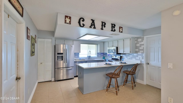 kitchen with a breakfast bar area, a peninsula, a sink, appliances with stainless steel finishes, and decorative backsplash