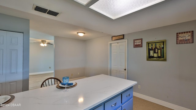 kitchen featuring ceiling fan, light stone counters, blue cabinets, visible vents, and baseboards