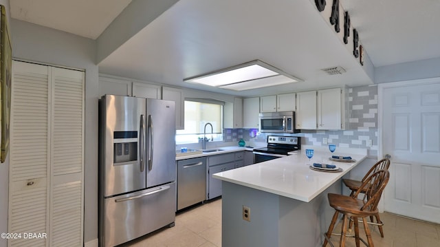 kitchen with sink, kitchen peninsula, a kitchen bar, decorative backsplash, and appliances with stainless steel finishes