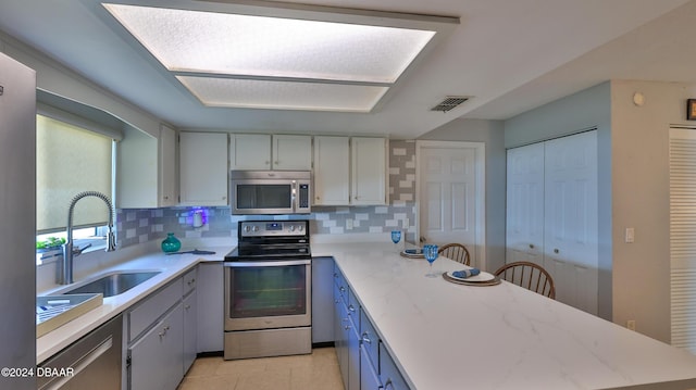 kitchen featuring stainless steel appliances, visible vents, decorative backsplash, a sink, and a peninsula