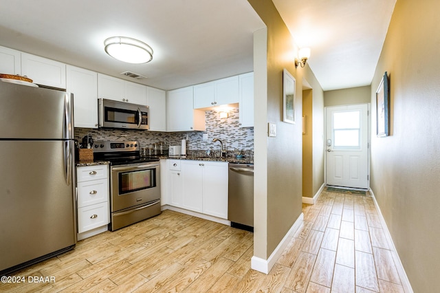 kitchen with white cabinetry, backsplash, appliances with stainless steel finishes, and light hardwood / wood-style flooring