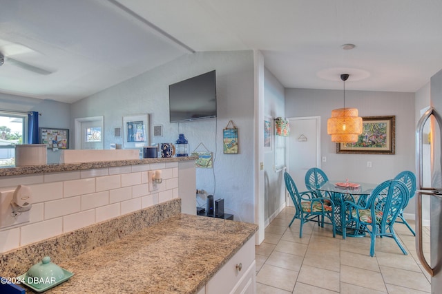 kitchen featuring stainless steel fridge, pendant lighting, light tile patterned floors, white cabinets, and lofted ceiling