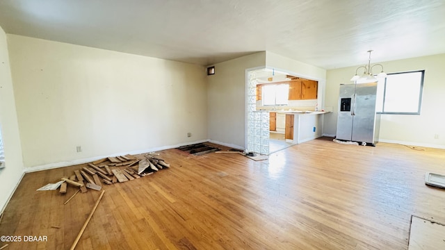 unfurnished living room with light wood-style floors, baseboards, and an inviting chandelier