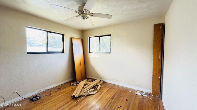 empty room with a wealth of natural light, hardwood / wood-style flooring, a textured wall, and ceiling fan