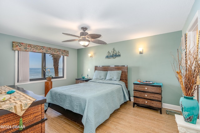 bedroom with light hardwood / wood-style floors, ceiling fan, and a water view