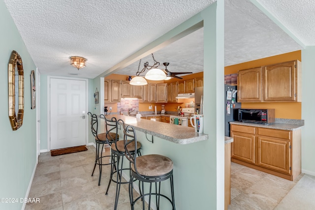 kitchen with electric stove, fridge, a breakfast bar, and a textured ceiling