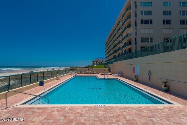 view of swimming pool with a water view, a patio area, and a view of the beach