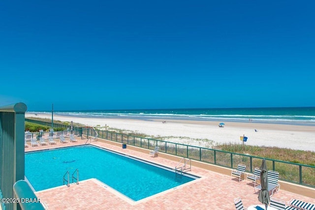 view of swimming pool featuring a water view, a beach view, and a patio