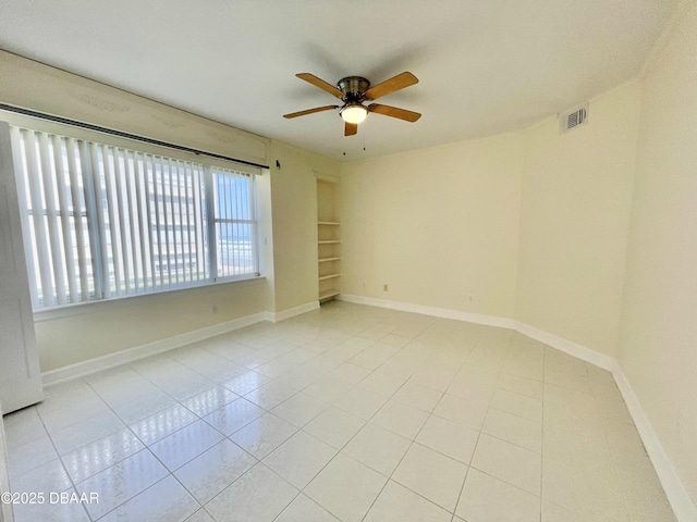 tiled spare room with ceiling fan and built in shelves