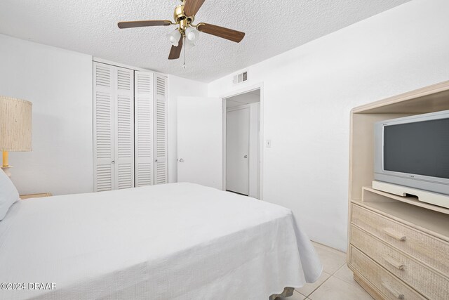 bedroom featuring a textured ceiling, a closet, ceiling fan, and light tile patterned floors