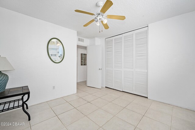 bedroom featuring a textured ceiling, light tile patterned floors, ceiling fan, and a closet