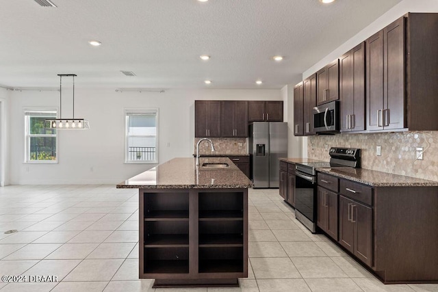 kitchen with a kitchen island with sink, sink, hanging light fixtures, appliances with stainless steel finishes, and tasteful backsplash