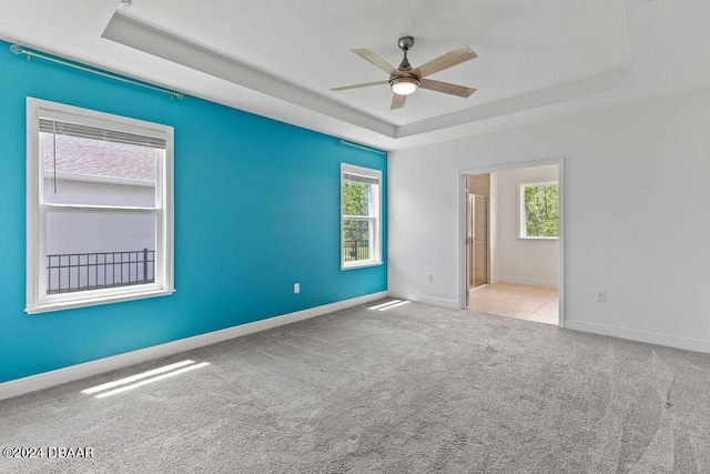 unfurnished room with a tray ceiling, light carpet, plenty of natural light, and ceiling fan