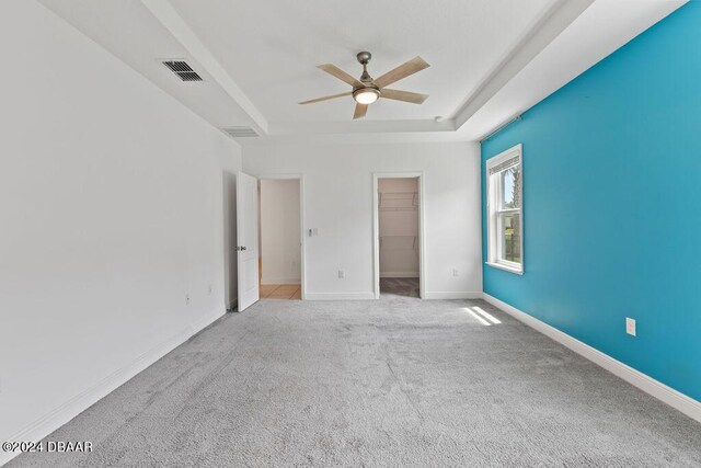 carpeted empty room with ceiling fan and a raised ceiling