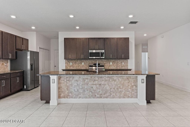 kitchen with dark stone countertops, a kitchen island with sink, sink, and stainless steel appliances