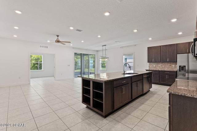 kitchen with pendant lighting, backsplash, a center island with sink, appliances with stainless steel finishes, and dark brown cabinets