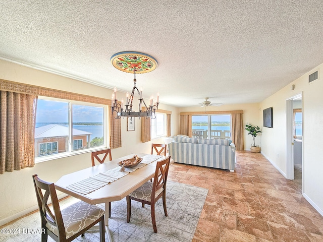 dining area with ceiling fan with notable chandelier, a textured ceiling, and a water view