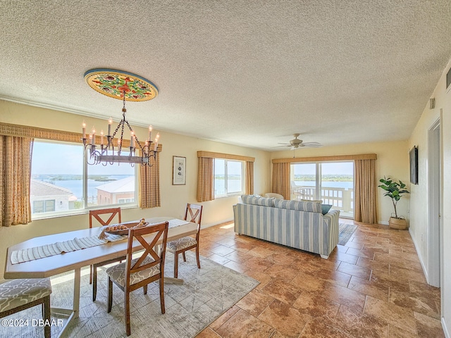 dining room featuring ceiling fan with notable chandelier, a textured ceiling, and a water view