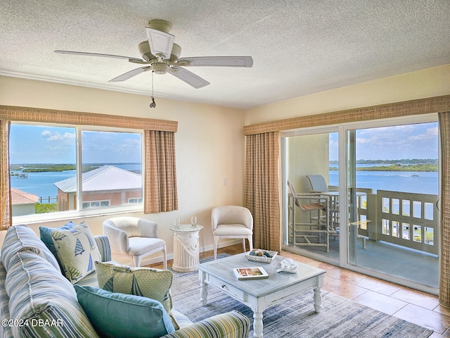 living room featuring ceiling fan, a water view, a textured ceiling, and a healthy amount of sunlight