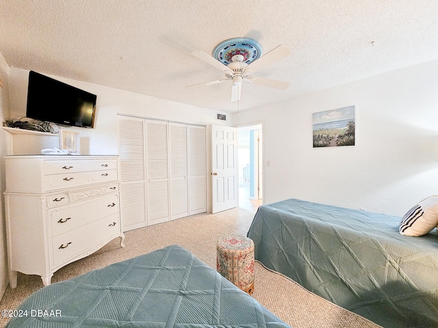 carpeted bedroom with a textured ceiling, ceiling fan, and a closet