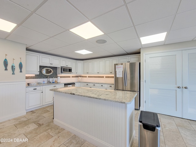 kitchen featuring stainless steel appliances, white cabinetry, light stone countertops, a drop ceiling, and a center island