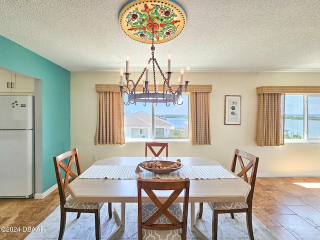 dining room featuring a wealth of natural light, a water view, a textured ceiling, and an inviting chandelier