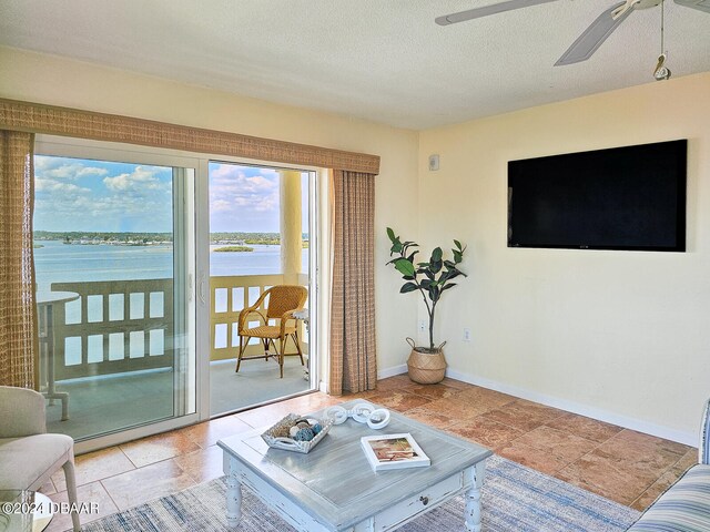 living room featuring a water view, a textured ceiling, and ceiling fan