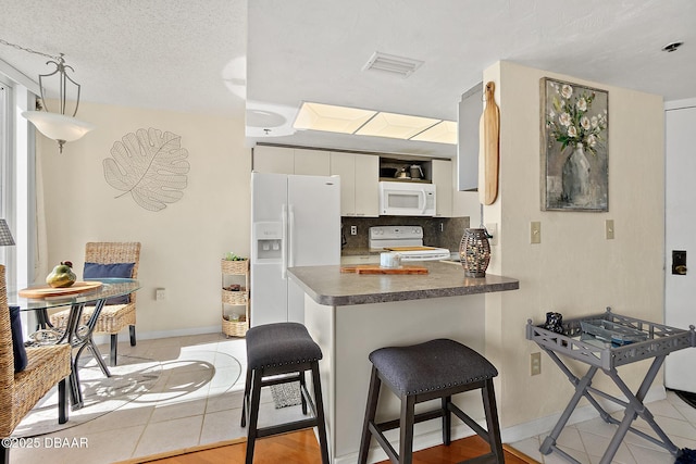 kitchen featuring light tile patterned flooring, white cabinetry, kitchen peninsula, white appliances, and decorative backsplash