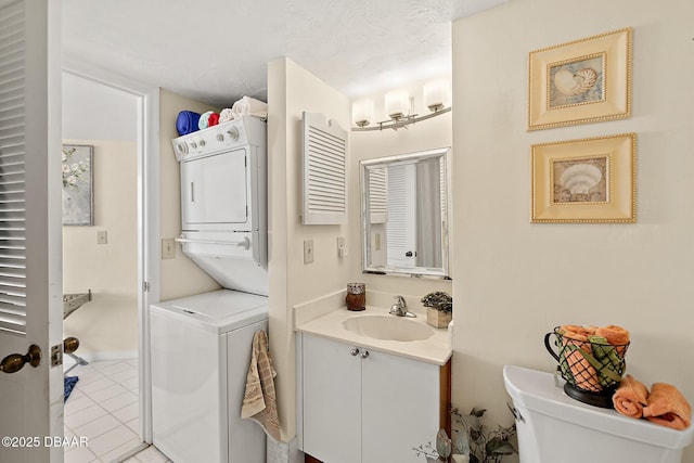 bathroom featuring stacked washer and dryer, vanity, toilet, and tile patterned floors