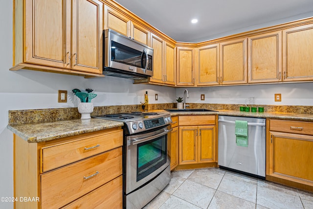 kitchen with appliances with stainless steel finishes, sink, light tile patterned floors, and stone countertops