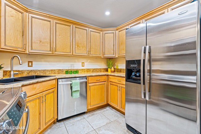 kitchen with appliances with stainless steel finishes, sink, light tile patterned flooring, and a textured ceiling