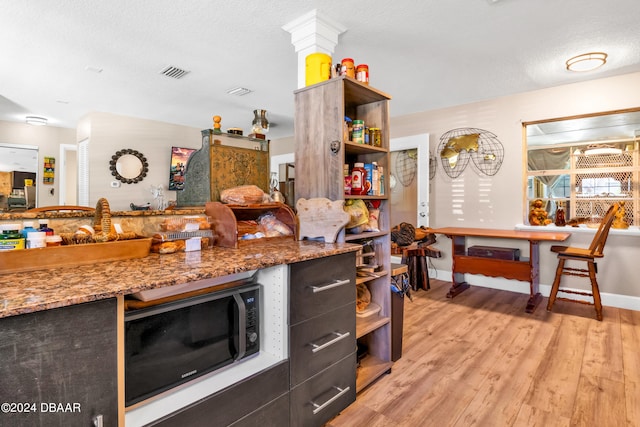 kitchen with ornate columns, stone counters, a textured ceiling, and light hardwood / wood-style floors