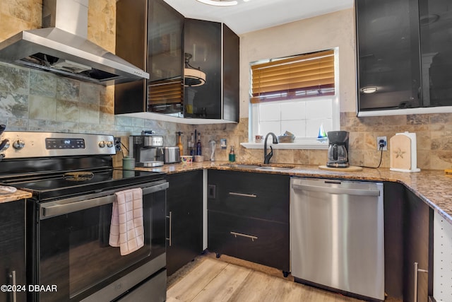 kitchen with stainless steel appliances, light stone countertops, sink, light hardwood / wood-style floors, and wall chimney exhaust hood