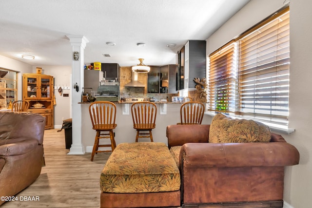 living room with light wood-type flooring, a textured ceiling, and decorative columns