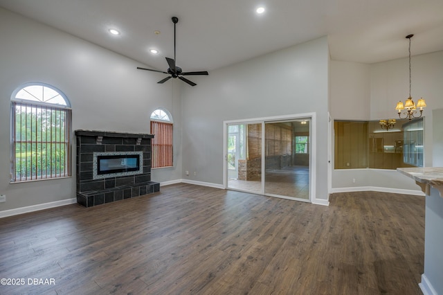 unfurnished living room featuring a high ceiling, dark wood-style flooring, ceiling fan with notable chandelier, and a wealth of natural light