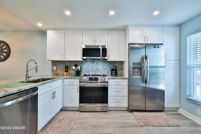 kitchen featuring light stone countertops, white cabinetry, sink, stainless steel appliances, and decorative backsplash