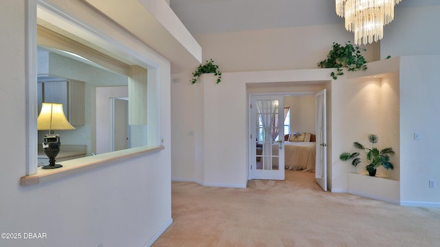 hall featuring baseboards, carpet, and a chandelier