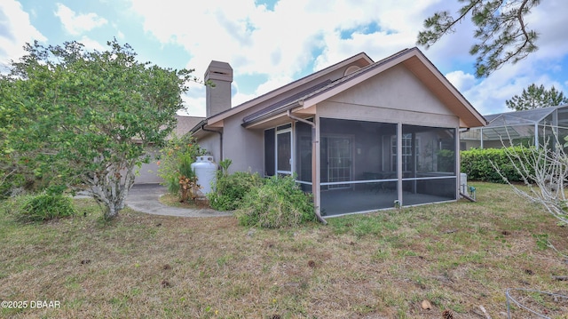 rear view of property with a lawn, a chimney, a sunroom, and stucco siding